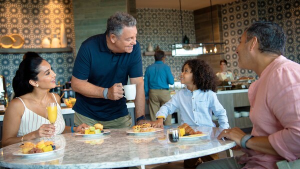Une famille est assise à une table et savoure des fruits, des muffins et des boissons