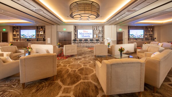 Small couches and chairs arranged in sections and a television screen showing the words ‘Disney Meetings and Events’