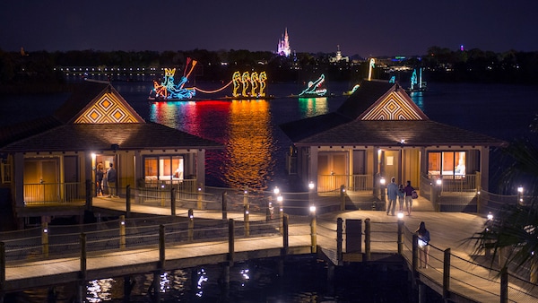 Des gens se tiennent sur les quais avec 2 bungalows près d’un lac et un défilé lumineux d’animaux aquatiques