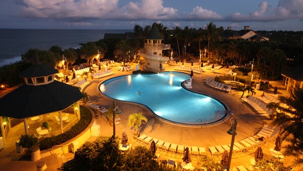 Evening lights illuminate the poolside area which features umbrellas, lounge chairs and a waterslide