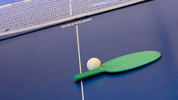 Primer plano de una paleta de ping pong y una pelota blanca sobre una mesa azul