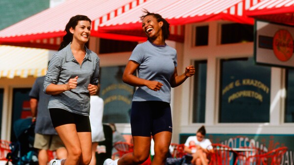 2 women enjoying a jog while passing a storefront with a red and white striped awning