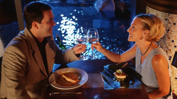 A man and a woman toast their glasses together at a table plated with food
