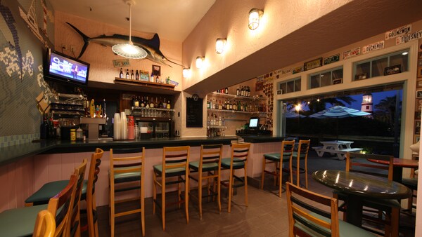 A bar with a seating area near a TV and a stuffed marlin with a picnic table and a lighthouse nearby outside