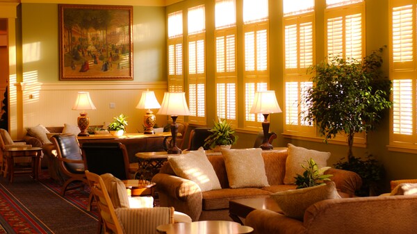 A desk, sofas and chairs in a sunlit sitting area next to a bank of windows