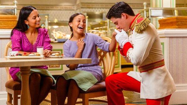 Una niña se ríe mientras una princesa le besa la mano y una mujer observa