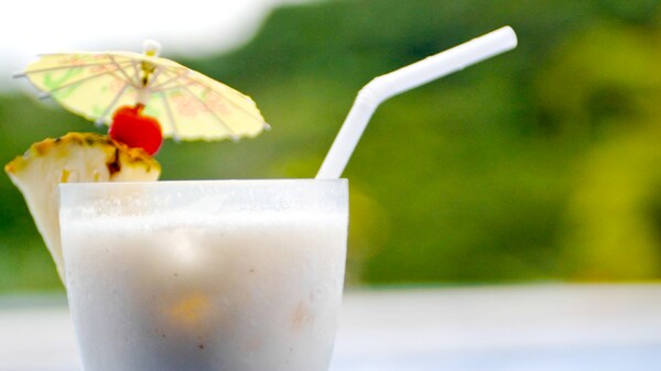 Un trago adornado con un trozo de piña, una cereza y una sombrilla