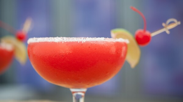Un trago con un vaso con sal en el borde, decorado con un limón verde y una cereza