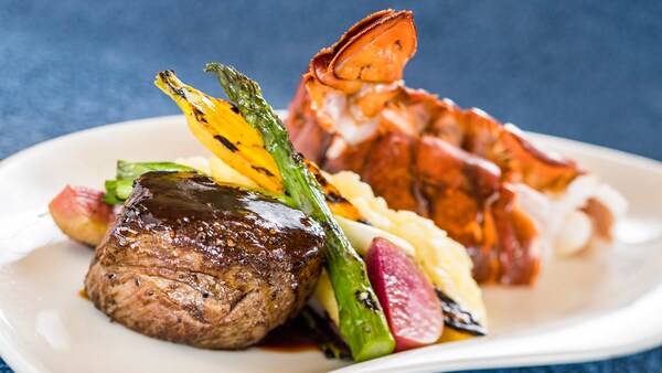 Tenderloin steak next to roasted asparagus, leak, squash, beat, cauliflower and 2 lobster tails on a plate