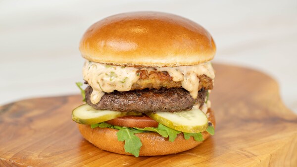Un hamburger avec laitue, tomate, cornichons, une galette de bœuf, un morceau de poisson frit et une sauce tartare