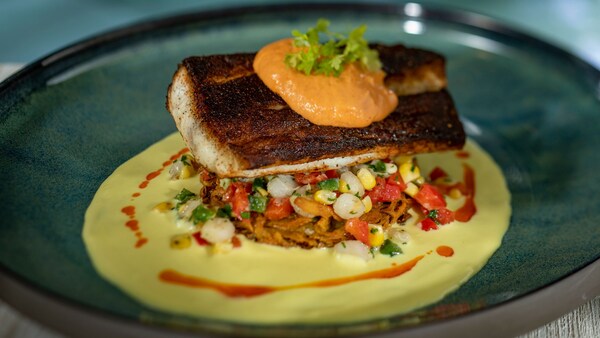 Un trozo de pescado servido con maíz y otros vegetales