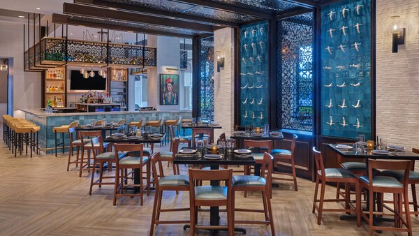 Un restaurante bar y área de comidas con decoración moderna y un mural con arte mexicano