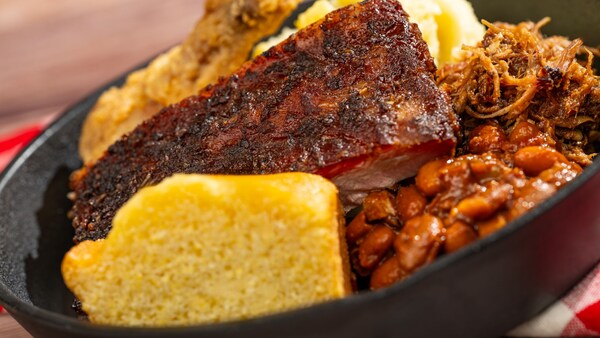 A skillet with smoked brisket, pulled pork, fried chicken, baked beans, mashed potatoes and cornbread