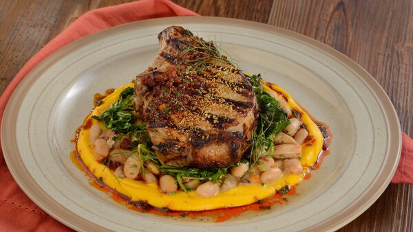 A grilled pork chop served over a bed of beans, greens and sweet potato puree