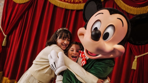 Two girls embracing Mickey at Mickey’s Very Merry Christmas Party  	