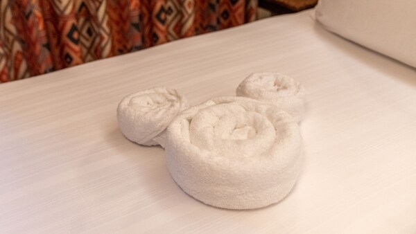 A set of 3 towels arranged in the shape of the head and ears of Mickey Mouse on a bed at Disney's Animal Kingdom Lodge