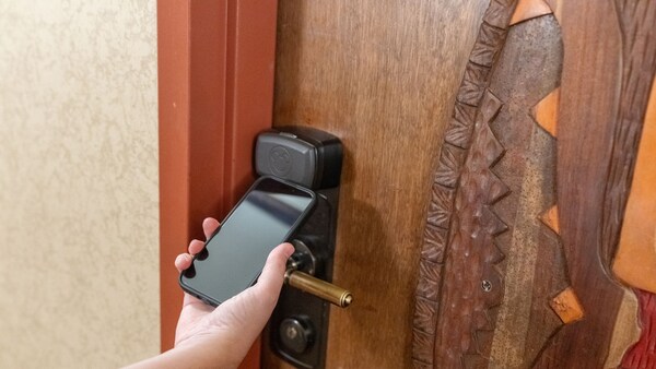 Una mano acerca un teléfono inteligente a la cerradura de la puerta de una habitación en Disney's Animal Kingdom Lodge	