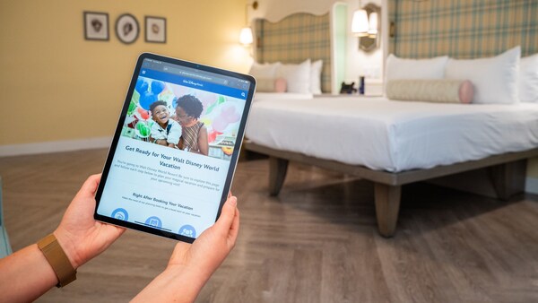Hands holding a tablet displaying the Walt Disney World Resort website in a room at Disney’s BoardWalk Inn