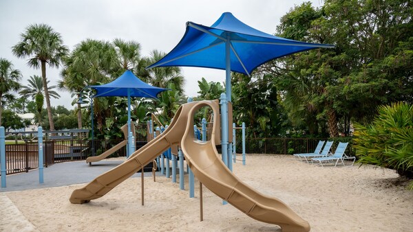 A playground at Disney’s Old Key West Resort, situated on sand and featuring slides, shade structures and lounge chairs