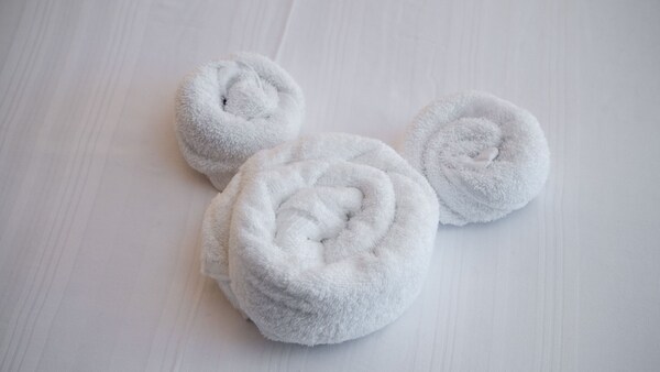 A set of 3 towels arranged in the shape of the head and ears of Mickey Mouse on a bed
