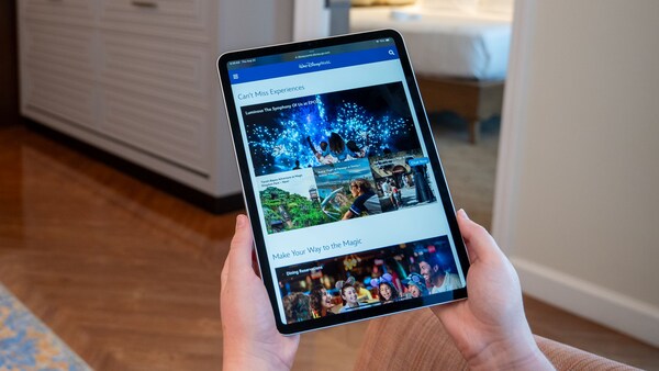 A hand holding a tablet displaying the Disney Parks website in a room at Disney’s Riviera Resort