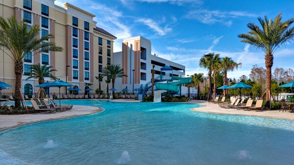 Una piscina de hotel rodeada de sillas reclinables, sombrillas y palmeras	
