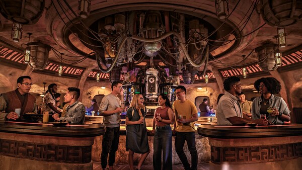 Adultos disfrutan bebidas exóticas dentro de una cantina de Star Wars que tiene cañerías, tubos y máquinas inusuales