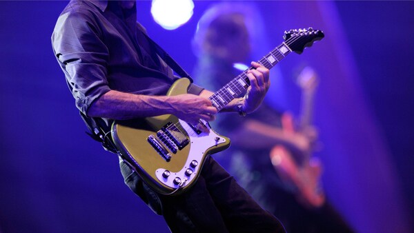 A guitarist performs on stage in the foreground alongside a fellow musician playing a bass guitar