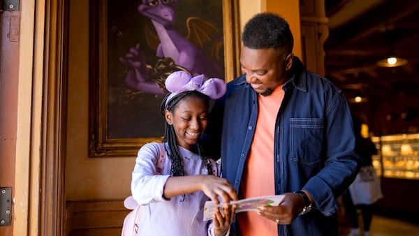A father and daughter looking at a Figment's Brush with the Masters Scavenger Hunt map near a framed Figment artwork