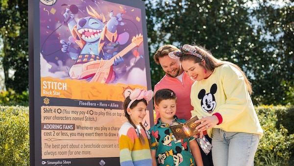 Four Guests playing the Disney Lorcana Trading Card Game beside a oversized Stitch trading card display at Walt Disney World Resort
