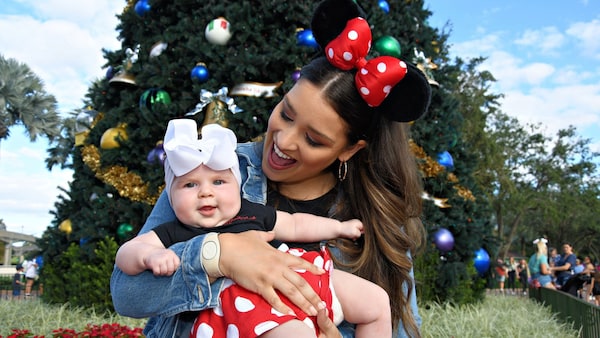 A mother holding her baby daughter in front of a Christmas tree at Epcot