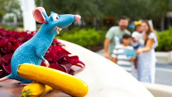A family of 4 looking at a Remy statuette placed on a table as part of the Remy's Ratatouille Hide & Squeak at Epcot International Food & Wine Festival