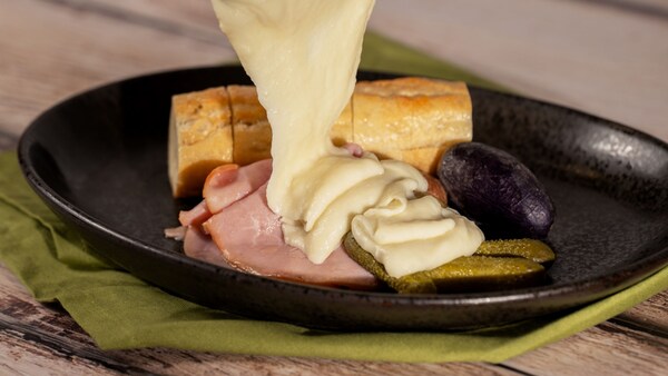 Un raclette tibio de queso suizo y jamón alpino con papas alargadas pequeñas, pepinillos y baguette de Emile’s Fromage Montage, en EPCOT