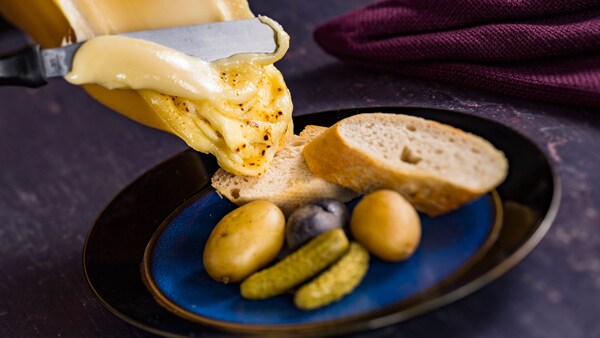 Un raclette tibio de queso suizo con papas alargadas pequeñas, pepinillos y baguette de Emile’s Fromage Montage, en EPCOT