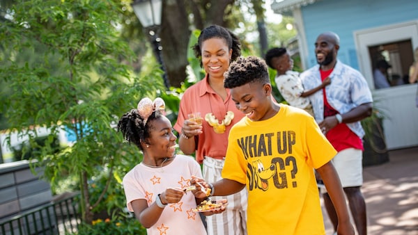 A family of 5 smiles while walking with food at EPCOT