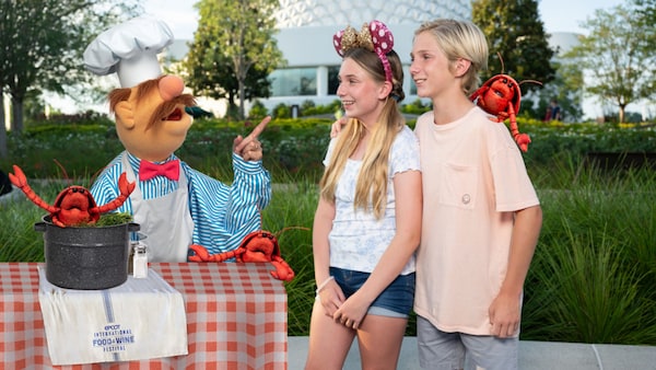 A boy and girl posing with the Swedish Chef and several lobster Muppets at Epcot