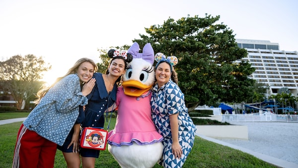 Trois visiteurs posent avec Daisy Duck devant l’hôtel contemporain de Disney