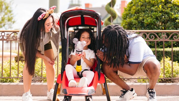 2 parents look on as their child beams from the seat of a rented stroller at Walt Disney World Resort