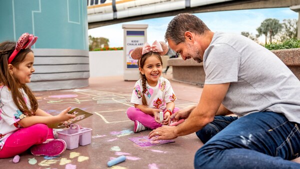 A father and his 2 daughters drawing with chalk on the ground near the Walt Disney World Monorail