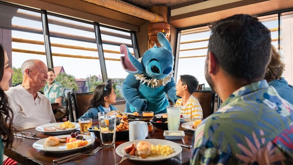 Stitch greets a family seated at a table eating breakfast in a restaurant