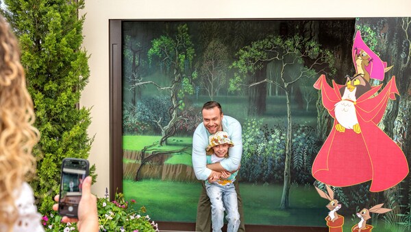 Un padre y su hija posan en un escalón en un marco con 4 animales del bosque animados de Sleeping Beauty