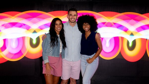 Tres amigos posando para una foto frente a una pared con un patrón de arco pintado con luz