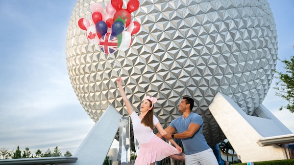 A Disney PhotoPass Magic Shot featuring 2 Guests holding Mickey Mouse balloons in front of Spaceship Earth at Epcot