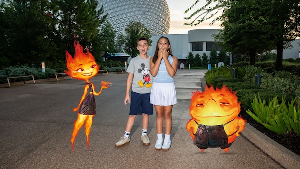 Two young kids posing for a photo at Epcot near illustrated overlays of characters from Elemental