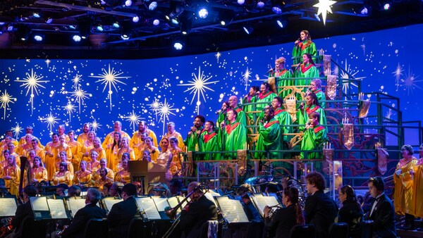 Cantantes con vestimenta con temática festiva y una orquesta tocando en Candlelight Processional en EPCOT