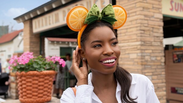 A Guest wearing an orange fruit themed Minnie Mouse ear headband in front of Anaheim Produce