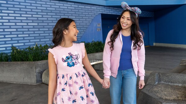 A girl in a Stitch themed dress holding hands with her mother, who wears a Minnie Mouse ear headband