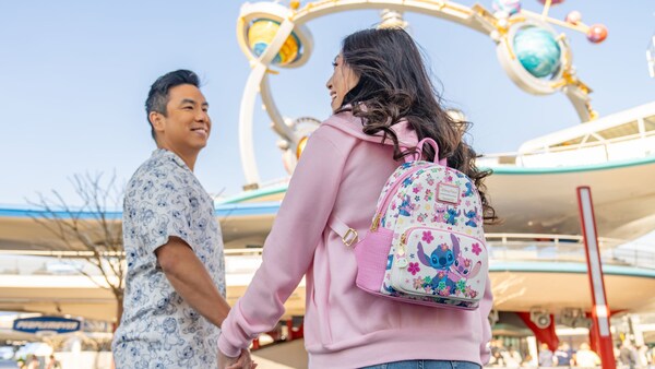 A couple wearing a Stitch themed short sleeved shirt and Loungefly backpack at Tomorrowland