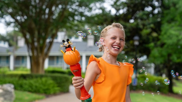 A child laughing while holding a Mickey Mouse pumpkin bubble wand at Walt Disney World Resort