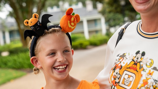 A child and adult in Halloween Minnie Mouse ears and Walt Disney World sweatshirt laughing together near a lakeside path